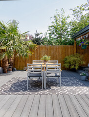 Minimalistic English modern garden with table and chairs. Sunny summers day with green plants and decking on the patio