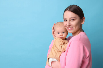 Happy mother with her cute baby on light blue background, space for text