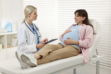Obraz premium Doctor with clipboard consulting smiling pregnant patient in clinic
