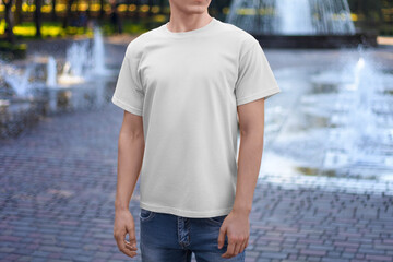Template of a white textured T-shirt on a guy, front view, for design, branding, on the background of a park, square.
