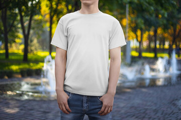 Template for a white summer T-shirt on a man in jeans, front view, for design, branding, on the background of a park, square,fountain.