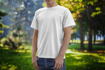 Mockup of a white T-shirt on a guy, on the background of a park, square, nature.