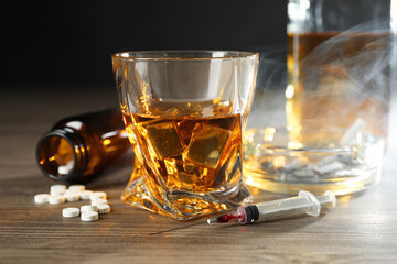 Alcohol and drug addiction. Whiskey in glass, syringe, pills and cigarettes on wooden table