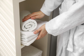 Woman stacking clean towels on shelf in bathroom, closeup