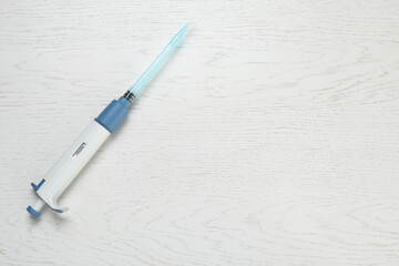 Laboratory analysis. Micropipette with liquid on white wooden table, top view. Space for text