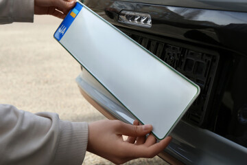 Woman installing vehicle registration plate outdoors, closeup