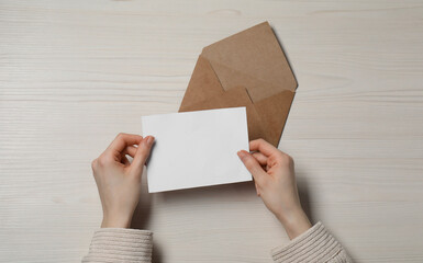 Woman with blank card at light wooden table, top view. Space for text