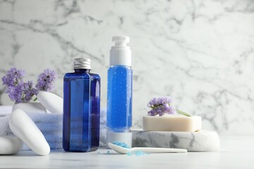Spa composition. Bottles of cosmetic products, sea salt, stones, soap and flowers on white marble table