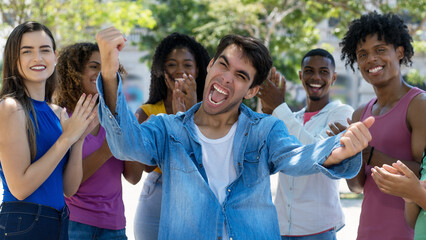 Successful cheering hispanic male young adult with group of applauding people
