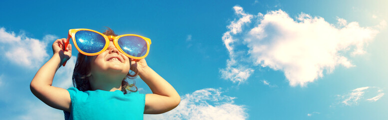 A little girl wearing big funny sunglasses enjoys the sun. Horizontal banner