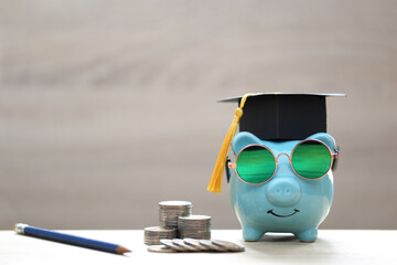 Graduation hat on blue piggy bank with stack of coins money on wooden background, Saving money for...