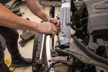 A man is working on a car engine, tightening a bolt with a wrench