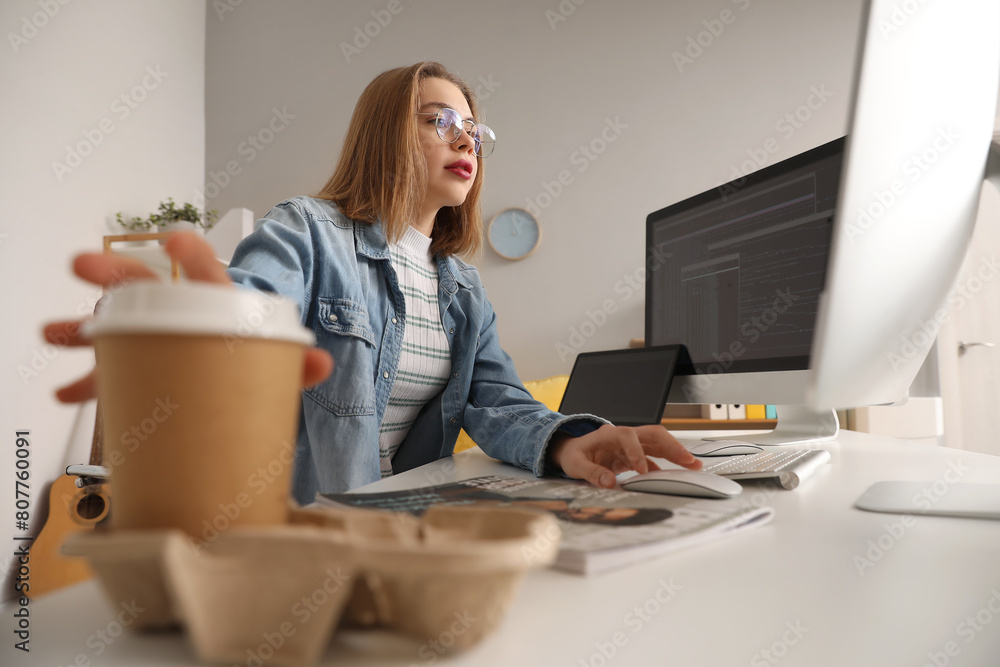 Poster female programmer taking cup of coffee from table in office