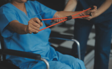 Personal trainer assisting senior woman with resistance band. Rehabilitation physiotherapy worker helping old patient at nursing home. Old woman with stretch band being coached by physiotherapist.