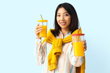Beautiful Asian woman with glasses of juice on blue background