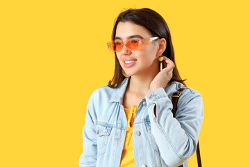 Beautiful young woman in stylish sunglasses on yellow background