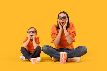 Beautiful mother and her cute little daughter in 3D glasses with buckets of popcorn on yellow...