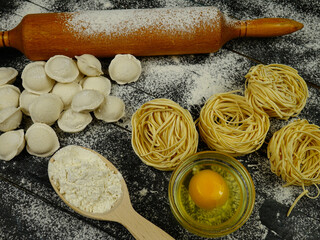Homemade ravioli and pasta, rolling pin, raw egg, flour lie on a floured wooden board