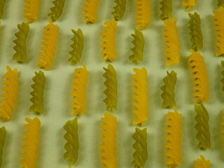 Italian uncooked green and yellow  pasta fusilli  are laid out in rows on light green fabric,...
