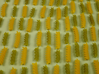 Italian uncooked green and yellow  pasta fusilli  are laid out in rows on light green fabric,...