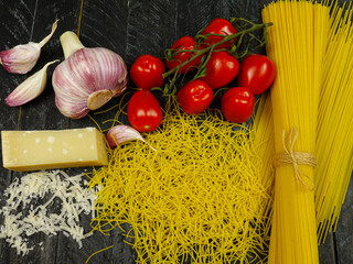 talian cuisine, traditional pasta and ingredients for it.  Cherry tomatoes, garlic, parmesan cheese, spaghetti and vermicelli are on a black cutting board
 - obrazy, fototapety, plakaty