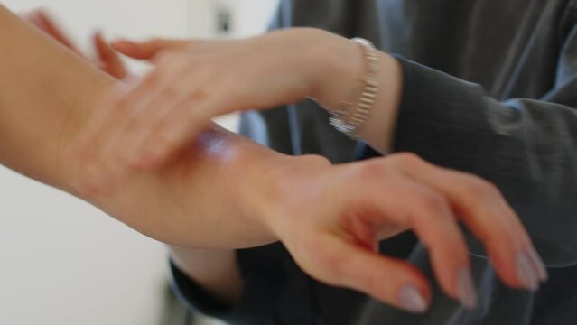 Cropped medium closeup of Caucasian fitness bikini model and her assistant using tanned bronzer on skin while getting ready for shooting commercial in studio
