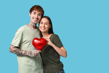 Young couple with heart-shaped air balloon on blue background