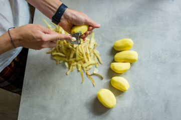 a man peeling potatoes on a grey kitchen counter with a potato peeler