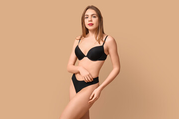 Fototapeta premium Sexy young woman in black underwear on beige background