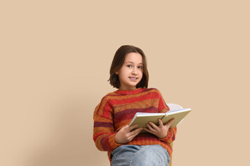 Little girl reading book while sitting on chair near beige wall