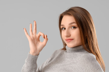 Young woman showing OK on light background