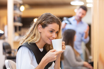 female customer in hairdressing salon enjoying a cup of coffee