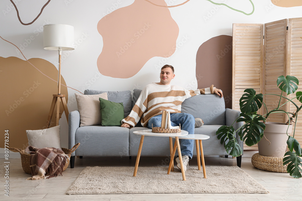 Poster Young man sitting on sofa in living room