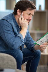man sitting doing crossword puzzle looking thoughtfully at a magazine