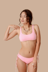 Naklejka premium Sexy young woman in pink swimsuit on beige background