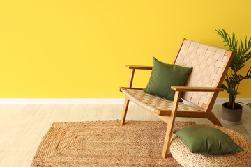 Interior of living room with armchair, footrest and cushions near yellow wall