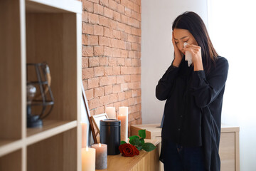Grieving young Asian woman with mortuary urn crying at funeral