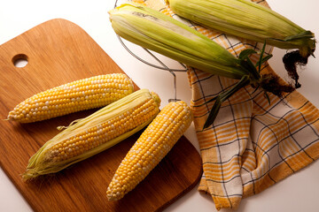 Cutting board with three cobs sweet corn on white wooden background..