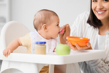 Mother feeding her little baby with puree at home, closeup