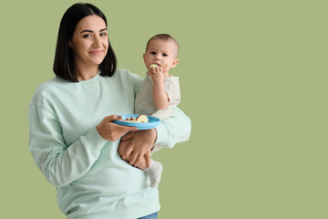 Young woman feeding her little baby with apple on green background