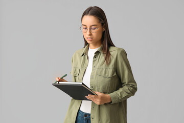 Young female writer with notebook on grey background