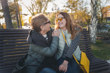 Two happy mature women friends mother and adult daughter communicate while sitting on a bench in...