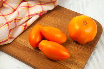 Cutting board with several yellow tomatoes and red kitchen towel on white wooden background..