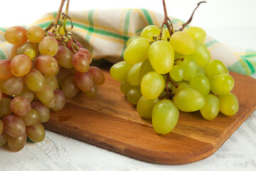 Cutting board with bunch of organic green and pink grapes on white wooden background..