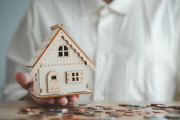 Housing finance, new home and home insurance concept. Hand holding house model and money coins....