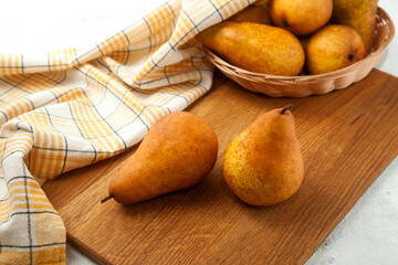 Cutting board with pears, wicker basket and yellow kitchen towel on white wooden background..
