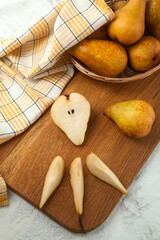 Cutting board with whole and slices pears, wicker basket and yellow kitchen towel on white wooden background..