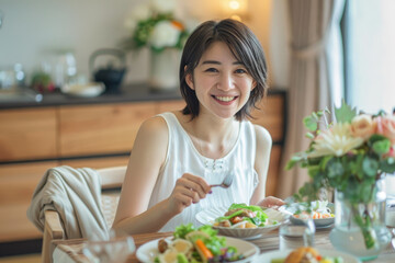 A Japanese woman in her thirties is smiling while eating, with short hair and wearing white. She is sitting at the dining table of an all-white modern minimalist kitchen