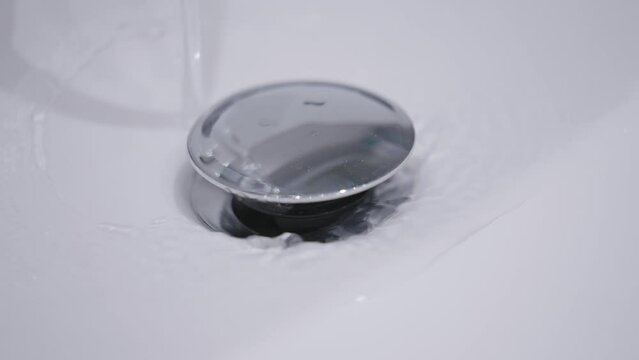 Water running continuously down sink drain. Close up, static shot.