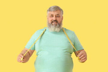 Overweight happy mature man with measuring tape on yellow background. Weight loss concept